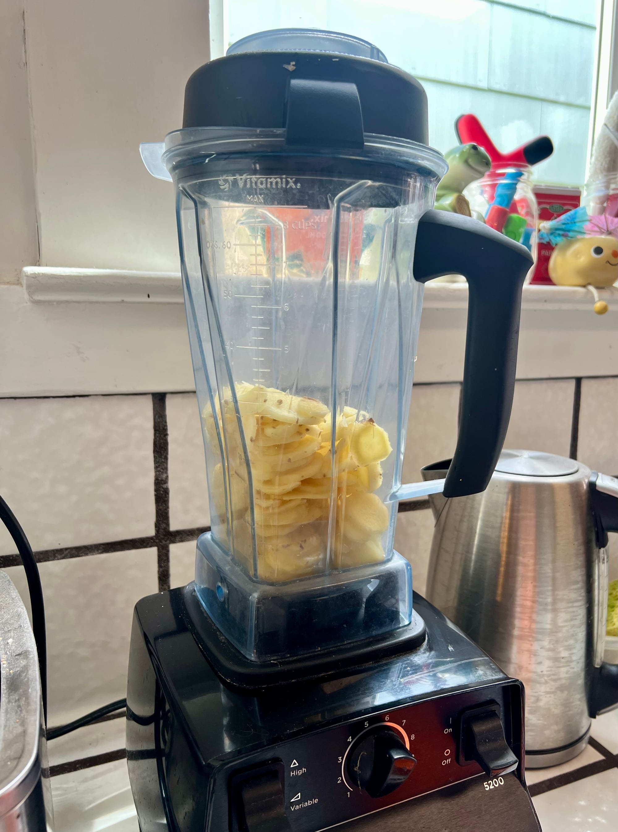 A Vitamix blender is about one-third full with thin slices of ginger.