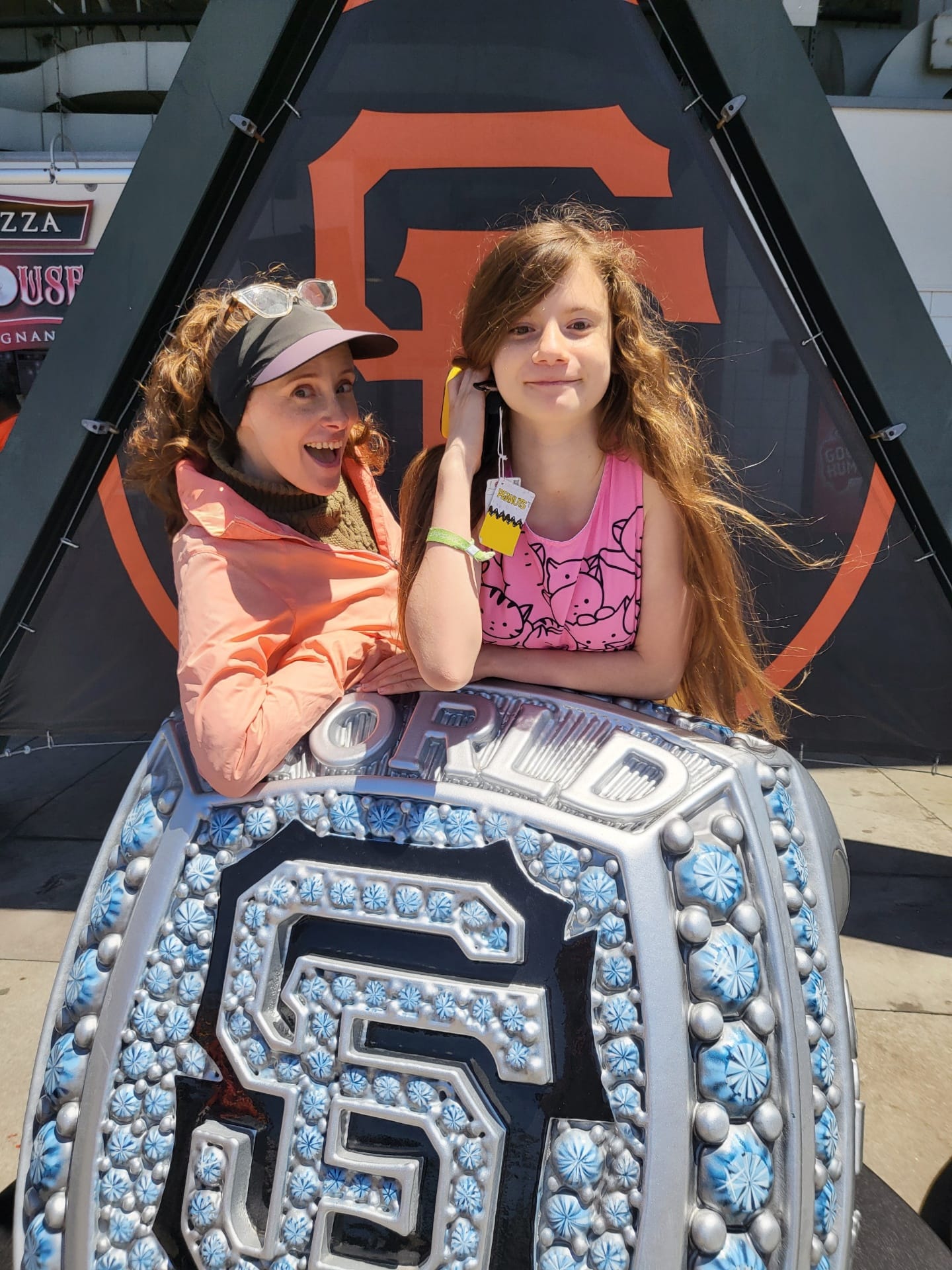 My daughter and I pose for a photo behind a giant model of an SF Giants World Series ring. My daughter is smirking oddly, to be a goof. I'm just a goof.