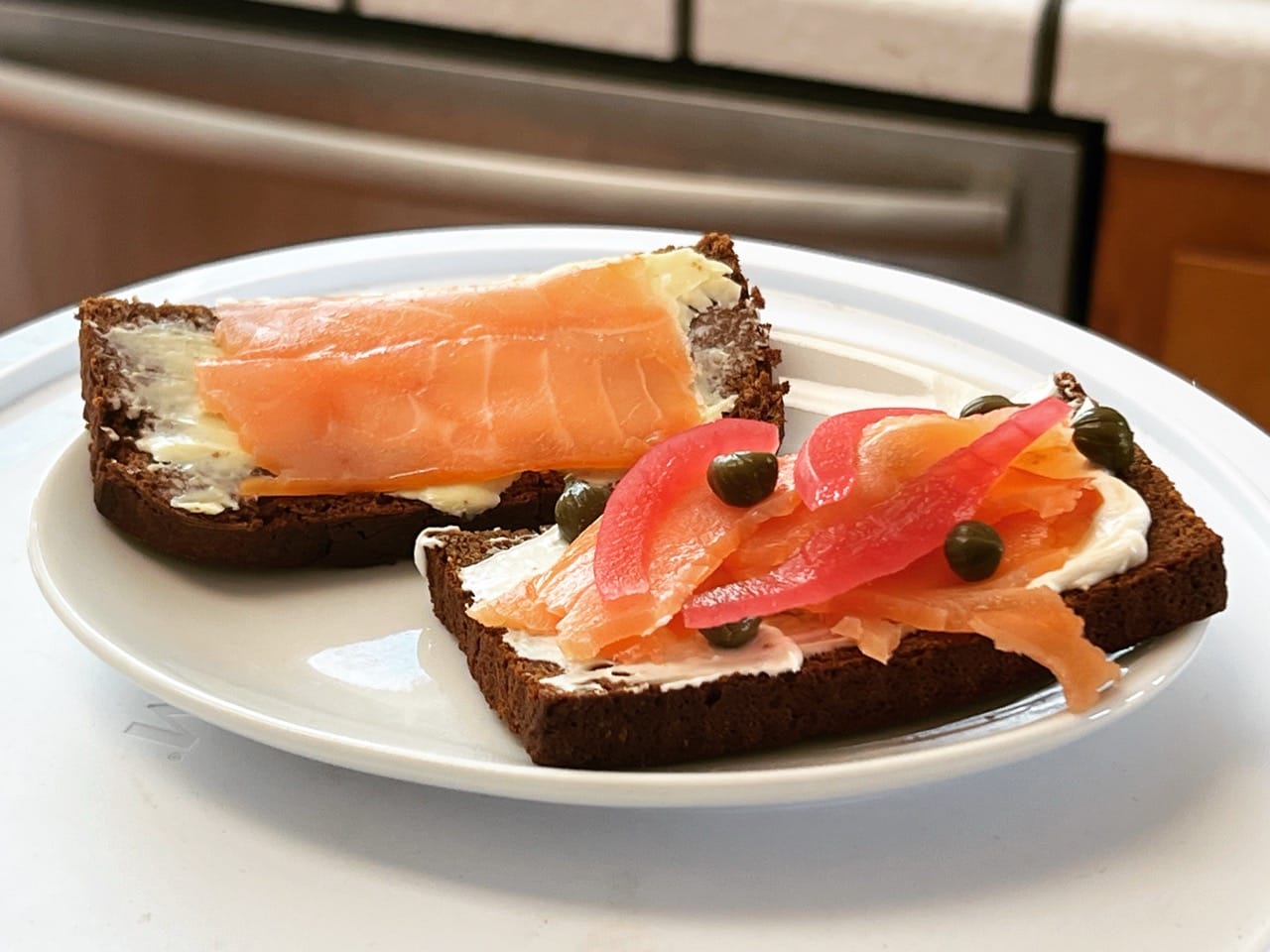 Open-face mini sandwiches made with dark rye bread, topped with cream cheese, smoked salmon, capers, and pickled red onions.